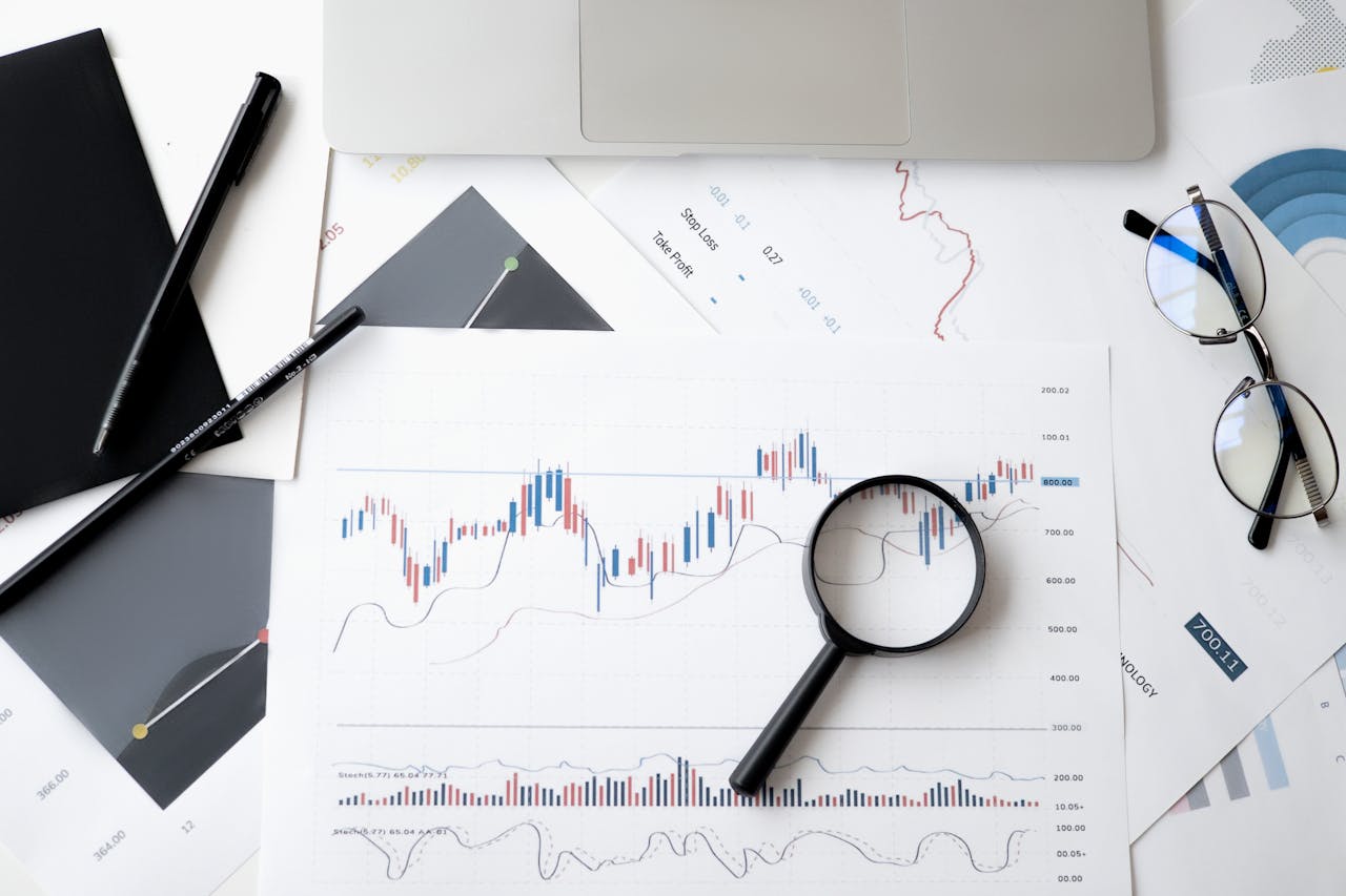 services-03 Flat lay of stock market analysis documents with magnifying glass, pens, and glasses.